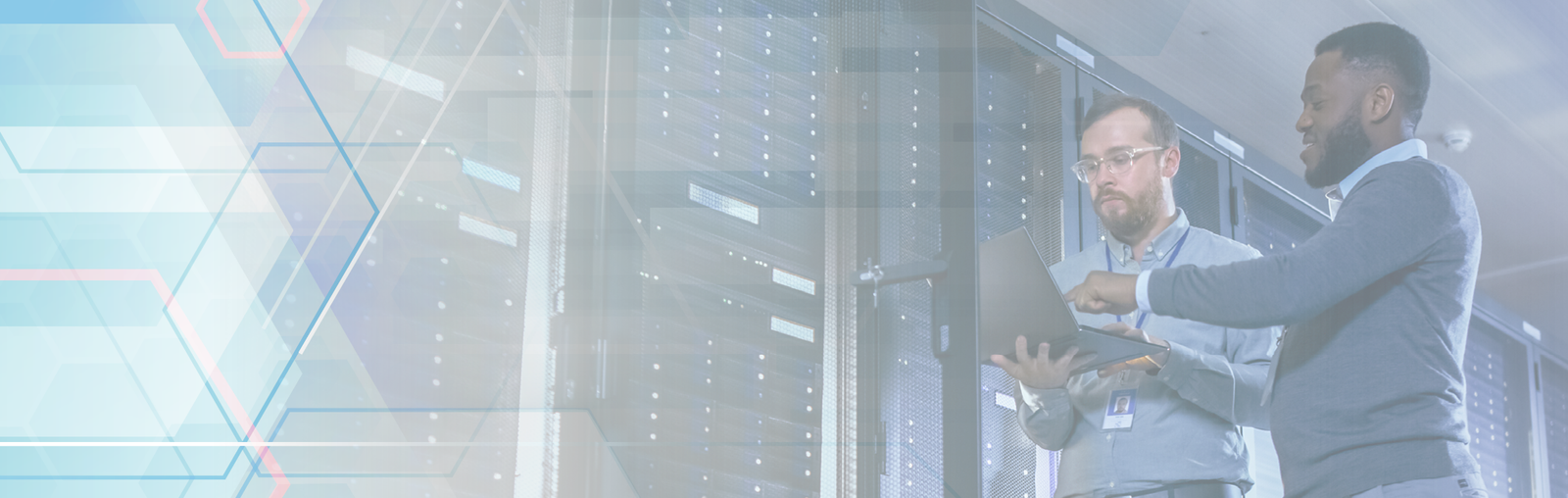 Two male IT professionals work on a laptop near a row of servers. One with dark hair and skin points to the screen while the other holds the laptop. The second man has light skin, brown hair and glasses. Both wear collared shirts and ID badges.