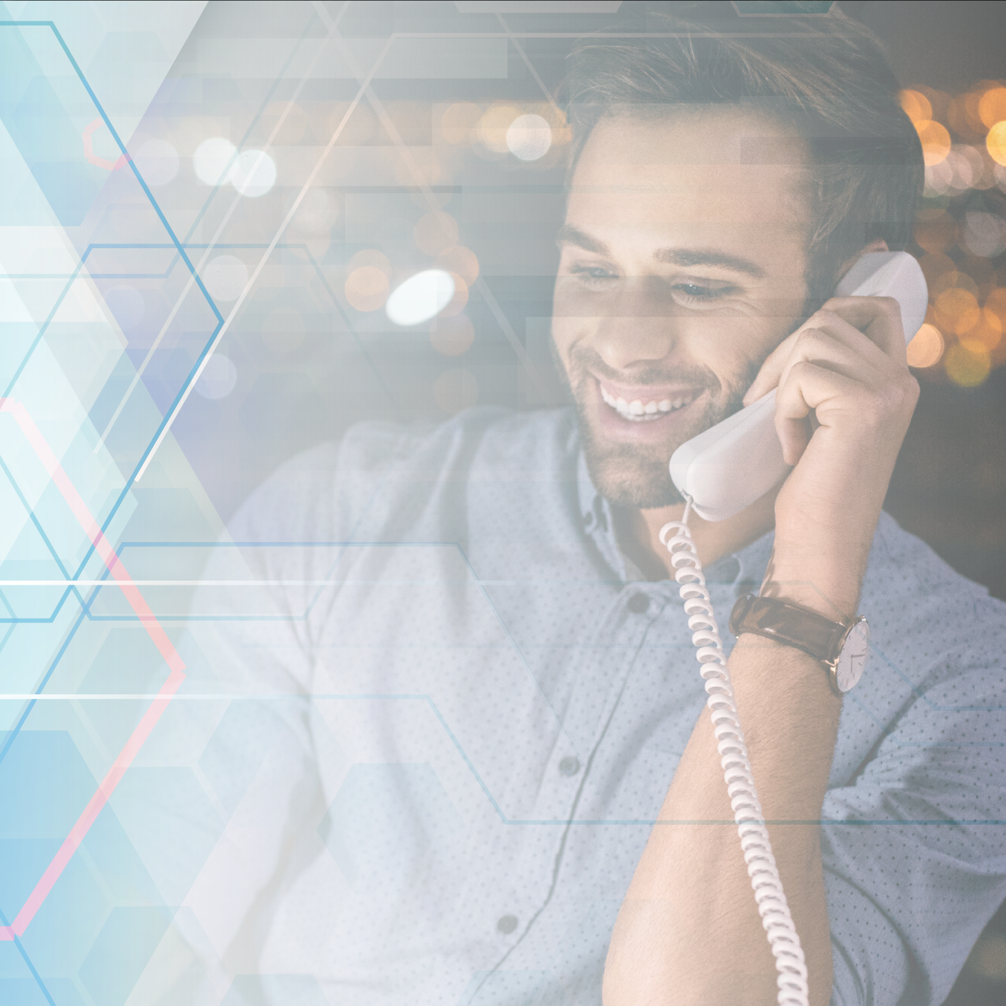 a young male professional smiles while talking on a SIP phone. He has brown hair, light skin and wears a blue collared shirt
